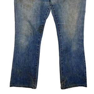 K&ouml;nnte beinhalten: Nahaufnahme einer blauen Jeanshose. Die Jeans hat ein verwaschenes Aussehen mit einigen Verf&auml;rbungen und Abnutzungserscheinungen. Die Hosenbeine sind unten leicht ausgestellt, und die N&auml;hte sind sichtbar.