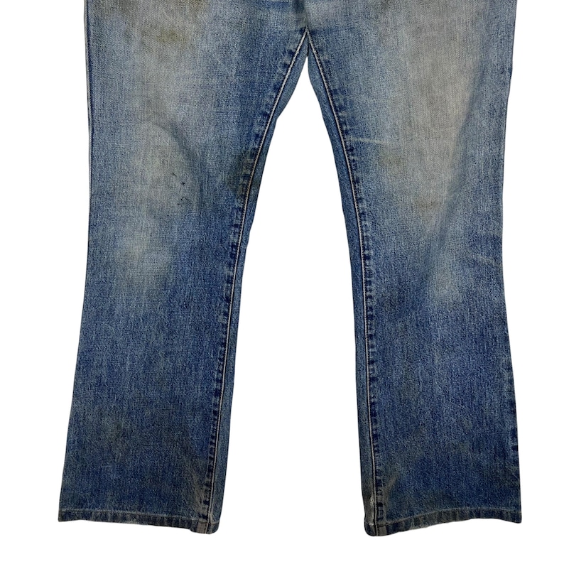 K&ouml;nnte beinhalten: Nahaufnahme einer blauen Jeanshose. Die Jeans hat ein verwaschenes Aussehen mit einigen Verf&auml;rbungen und Abnutzungserscheinungen. Die Hosenbeine sind unten leicht ausgestellt, und die N&auml;hte sind sichtbar.