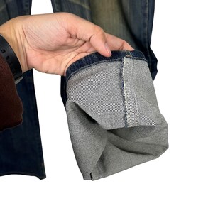 K&ouml;nnte beinhalten: Nahaufnahme des Saums einer blauen Jeans. Die Jeans ist hochgekrempelt und zeigt die Innenseite des Denim-Stoffs. Der Denim hat eine klassische blaue Farbe mit einem verblichenen Aussehen.
