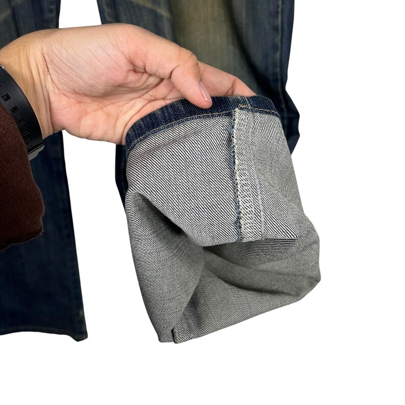 K&ouml;nnte beinhalten: Nahaufnahme des Saums einer blauen Jeans. Die Jeans ist hochgekrempelt und zeigt die Innenseite des Denim-Stoffs. Der Denim hat eine klassische blaue Farbe mit einem verblichenen Aussehen.
