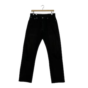 May include: Black denim jeans hanging on a wooden hanger. The jeans have a classic five-pocket design with a button and zipper closure. The pants are a solid black color.