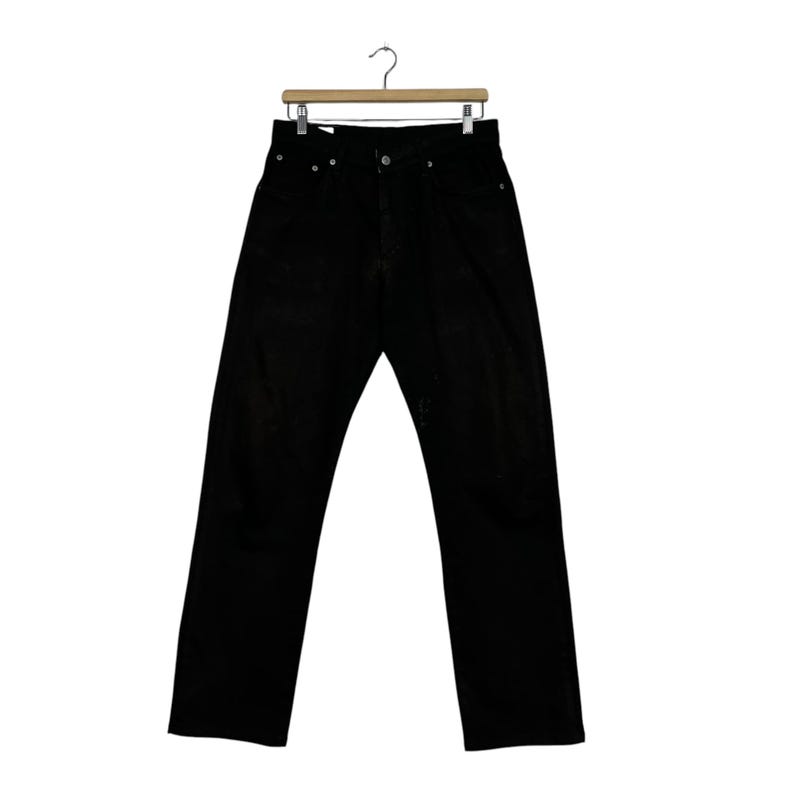 May include: Black denim jeans hanging on a wooden hanger. The jeans have a classic five-pocket design with a button and zipper closure. The pants are a solid black color.