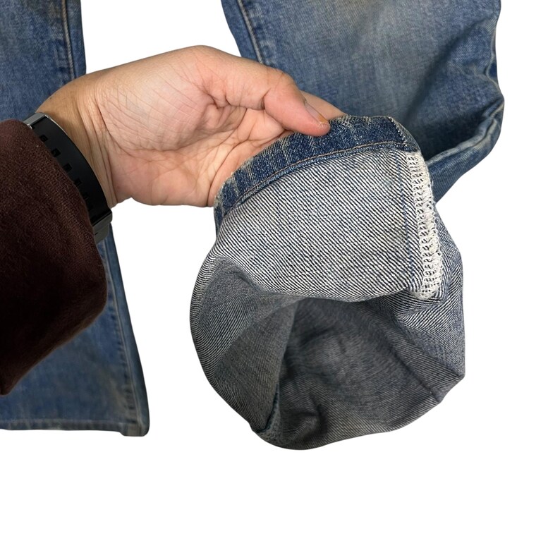 K&ouml;nnte beinhalten: Nahaufnahme einer hellblauen Jeans. Der Saum der Jeans ist hochgekrempelt und zeigt den Innenstoff und die N&auml;hte. Die Jeans ist abgenutzt und hat ein verwaschenes Aussehen.