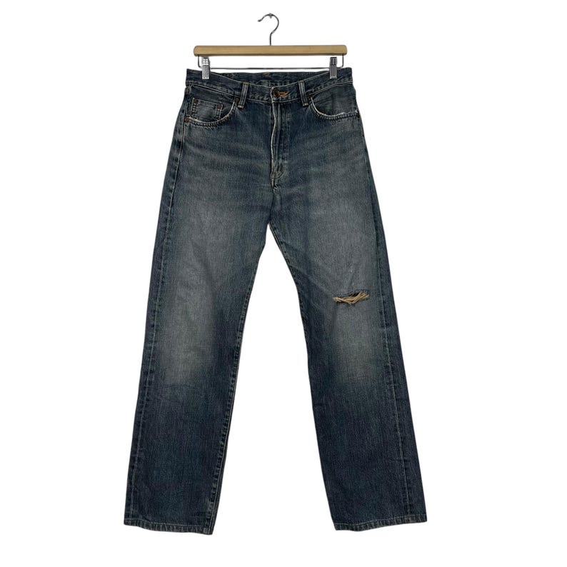 May include: A pair of blue denim jeans with a distressed knee. The jeans have a straight leg and a relaxed fit.