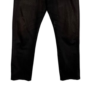 May include: A pair of black denim jeans. The jeans have a classic five-pocket design and a straight leg fit. The fabric appears slightly faded and worn, with some light discoloration near the right pocket. The jeans are displayed against a white background.