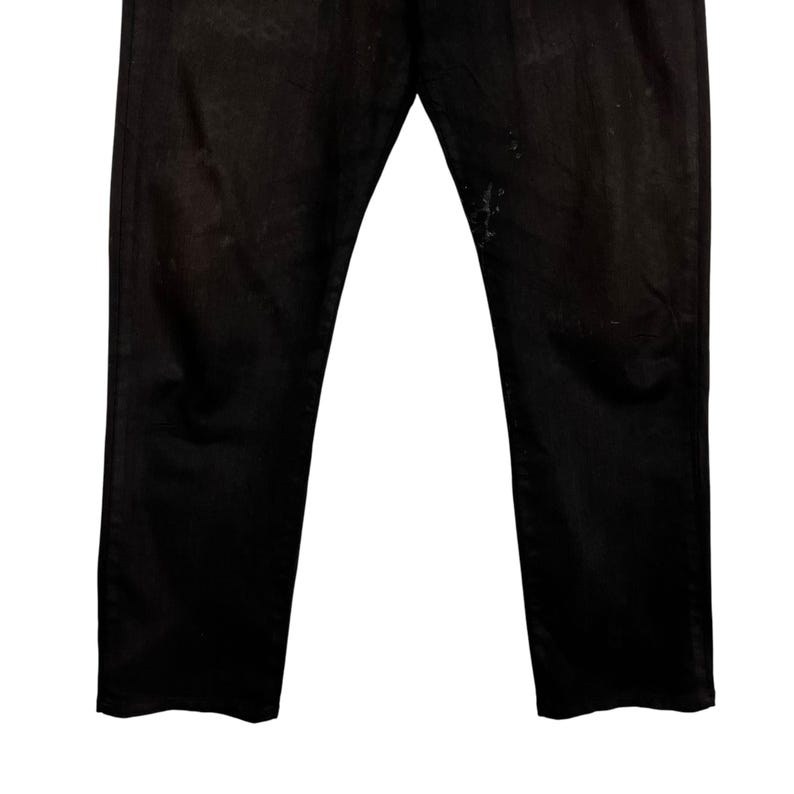 May include: A pair of black denim jeans. The jeans have a classic five-pocket design and a straight leg fit. The fabric appears slightly faded and worn, with some light discoloration near the right pocket. The jeans are displayed against a white background.