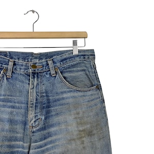 K&ouml;nnte beinhalten: Nahaufnahme einer verblichenen blauen Jeans, die an einem Holzb&uuml;gel h&auml;ngt. Die Jeans weist Gebrauchsspuren mit leichten Abnutzungen und Verf&auml;rbungen auf. Die Jeans hat ein klassisches F&uuml;nf-Taschen-Design.