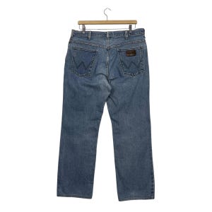 K&ouml;nnte beinhalten: Hellblaue Jeans aus Denim mit klassischem F&uuml;nf-Taschen-Design. Die Jeans haben einen braunen Lederaufn&auml;her auf der Ges&auml;&szlig;tasche und h&auml;ngen an einem Holzb&uuml;gel. Die Jeans haben eine mittlere Waschung.