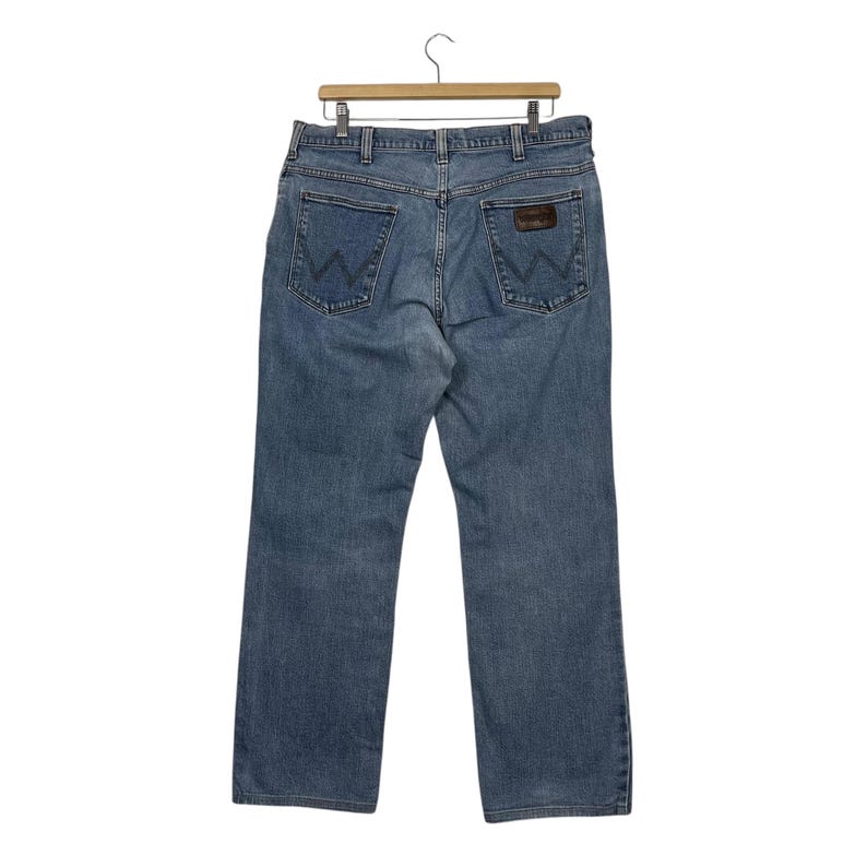 K&ouml;nnte beinhalten: Hellblaue Jeans aus Denim mit klassischem F&uuml;nf-Taschen-Design. Die Jeans haben einen braunen Lederaufn&auml;her auf der Ges&auml;&szlig;tasche und h&auml;ngen an einem Holzb&uuml;gel. Die Jeans haben eine mittlere Waschung.