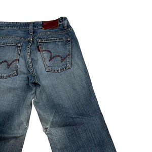 Op de afbeelding: Verbleekte blauwe spijkerbroek met rode stiksels op de achterzakken en een bruine leren patch. De jeans heeft een klassiek ontwerp met vijf zakken en een relaxte pasvorm. De denim heeft een versleten look.