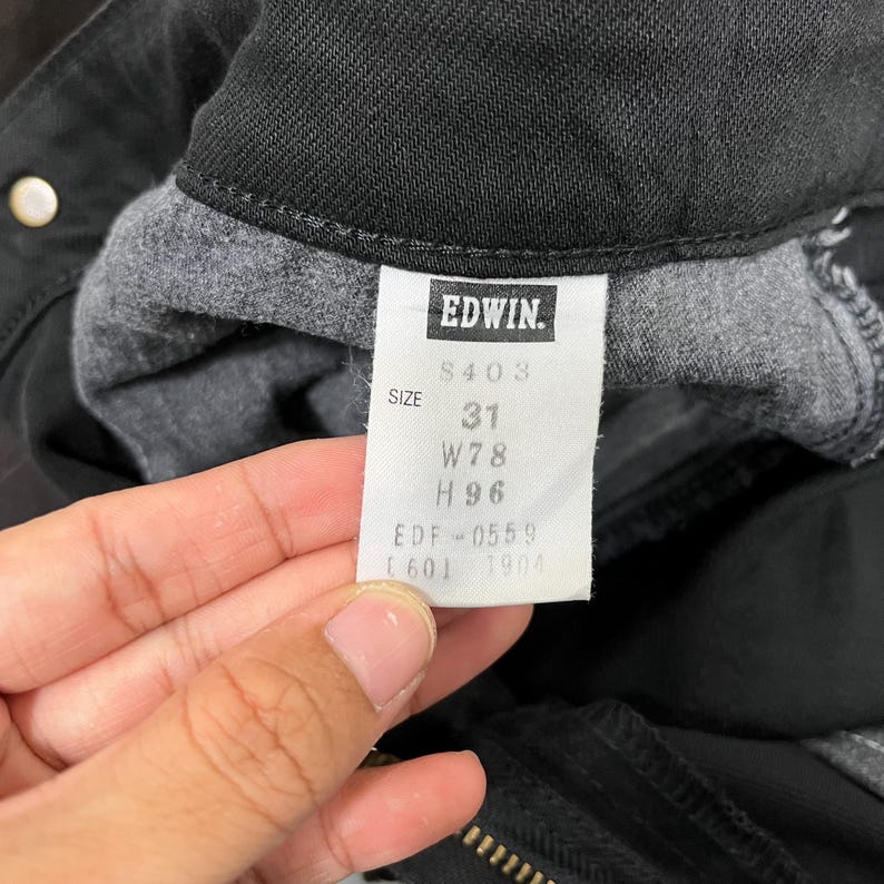 May include: Close-up of a black pair of Edwin jeans. The tag displays the brand name, size 31, and measurements W78 and H96. The jeans are folded, revealing the interior fabric.