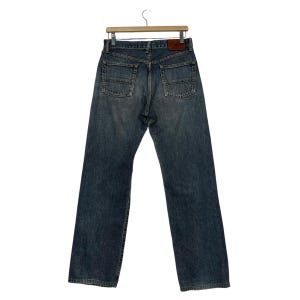 May include: A pair of blue denim jeans with a straight leg fit. The jeans have a brown leather patch on the back waistband.