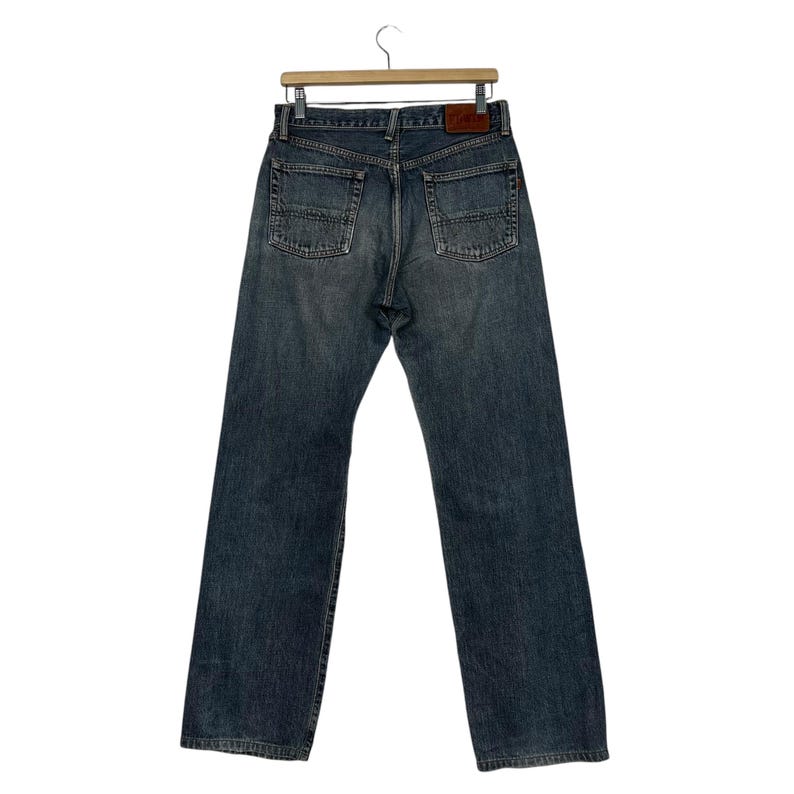 May include: A pair of blue denim jeans with a straight leg fit. The jeans have a brown leather patch on the back waistband.