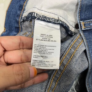 K&ouml;nnte beinhalten: Nahaufnahme eines Jeans-Etiketts. Auf dem Etikett steht "MADE IN USA 100% COTTON CUT# 108 STYLE# M24-BS-MILES". Waschhinweise sind ebenfalls aufgef&uuml;hrt. Die Jeans ist blau mit sichtbaren N&auml;hten.