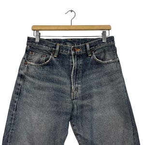 May include: A pair of dark blue denim jeans with a faded look. The jeans have a classic five-pocket style and a straight leg.
