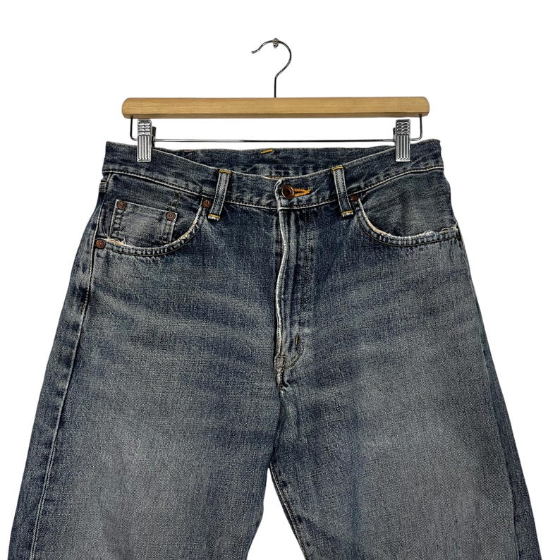 May include: A pair of dark blue denim jeans with a faded look. The jeans have a classic five-pocket style and a straight leg.