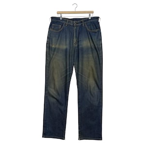 K&ouml;nnte beinhalten: Blaue Jeans aus Denim mit verwaschener Optik, h&auml;ngen an einem Holzb&uuml;gel. Die Jeans haben ein klassisches F&uuml;nf-Taschen-Design und einen geraden Beinverlauf. Der Denim hat ein abgenutztes Aussehen mit helleren Bereichen.