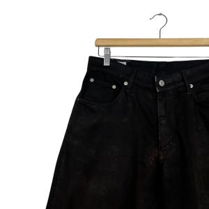 May include: Close-up of black denim jeans hanging on a wooden hanger. The jeans have a classic five-pocket design with a button and zipper closure. The fabric appears slightly faded, adding a vintage look.