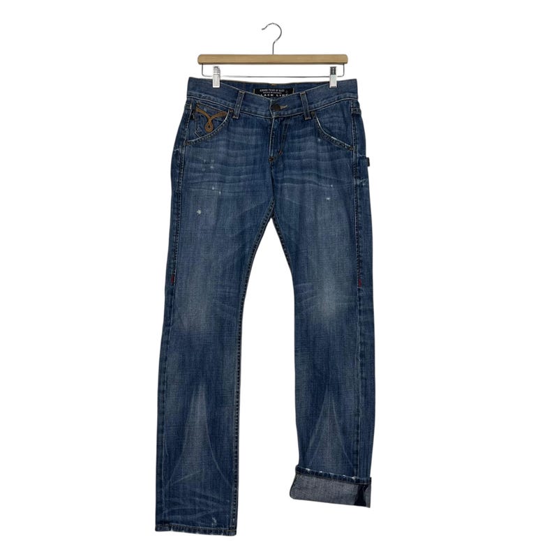 K&ouml;nnte beinhalten: Blaue Jeans aus Denim mit verwaschener Optik, klassischem F&uuml;nf-Taschen-Design und geradem Bein. Die Jeans h&auml;ngen an einem Holzkleiderb&uuml;gel. Die Manschetten sind hochgekrempelt und es gibt dezente Used-Details.