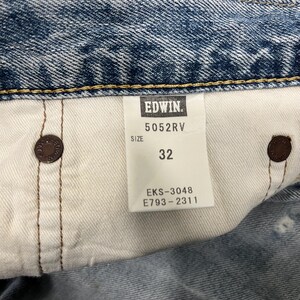 May include: Close-up of a pair of blue denim jeans with a white tag. The tag reads "EDWIN" and "5052RV" with a size of "32". The jeans have brown metal buttons and visible stitching.