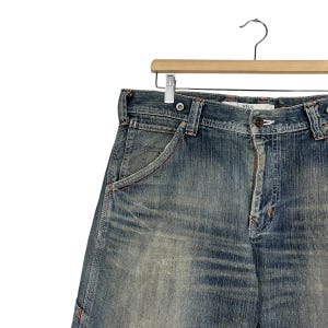 May include: Faded blue denim shorts with a classic five-pocket design. The shorts have a button closure, belt loops, and a small coin pocket. The denim has a worn, distressed appearance.