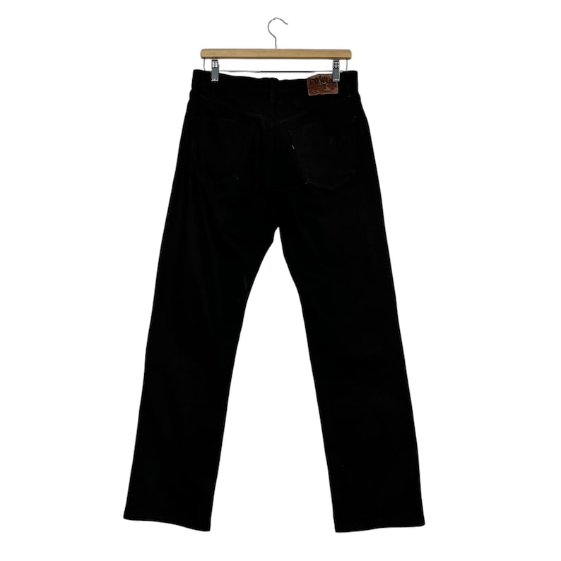 May include: Black corduroy pants hanging on a wooden hanger. The pants have a classic five-pocket design and a leather patch on the back. The pants are a solid black color.