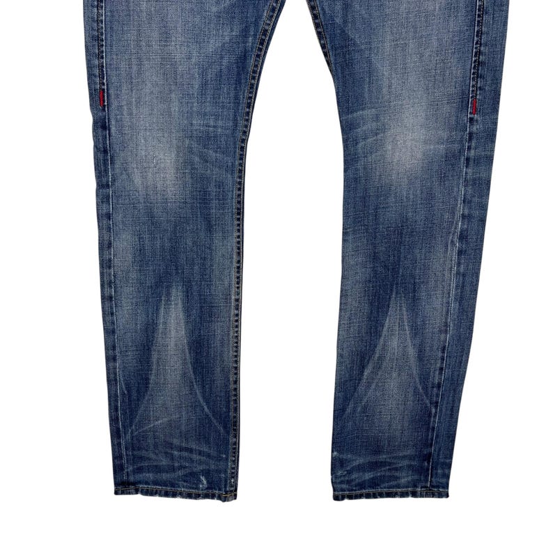 K&ouml;nnte beinhalten: Verblasste blaue Jeans aus Denim mit klassischem F&uuml;nf-Taschen-Design. Die Jeans haben einen geraden Beinverlauf und weisen subtile Abnutzungsmuster auf. Rote N&auml;hte akzentuieren die N&auml;hte.