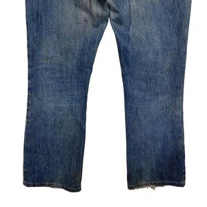 K&ouml;nnte beinhalten: Verblasste blaue Jeans mit leichtem Bootcut. Die Jeans weisen Abnutzungserscheinungen auf, mit Verf&auml;rbungen und ausgefransten Kanten am unteren Saum. Der Denim hat einen klassischen, Vintage-Look.