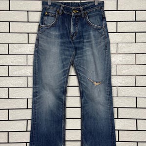 May include: Faded blue denim jeans with a distressed knee detail, hanging on a wooden hanger. The jeans have a classic five-pocket design and a slightly flared leg. The denim shows signs of wear and fading.