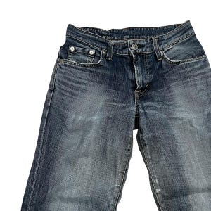 Op de afbeelding: Verbleekte blauwe denim jeans met een klassiek ontwerp met vijf zakken. De jeans hebben een knoop- en ritssluiting, met klinknagels op de voorzakken. De denim heeft een versleten uiterlijk met subtiele vervaging en slijtage.