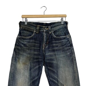 May include: Dark wash denim jeans hanging on a wooden hanger. The jeans have a classic five-pocket design, a button and zipper closure, and show signs of wear with faded areas and subtle distressing. The jeans are a medium rise and have a straight leg.