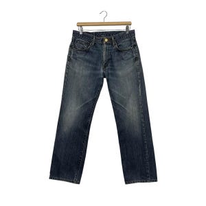 May include: Dark wash denim jeans hanging on a wooden hanger. The jeans feature a classic five-pocket design, a button and zip closure, and a straight leg fit. The denim has a faded appearance.