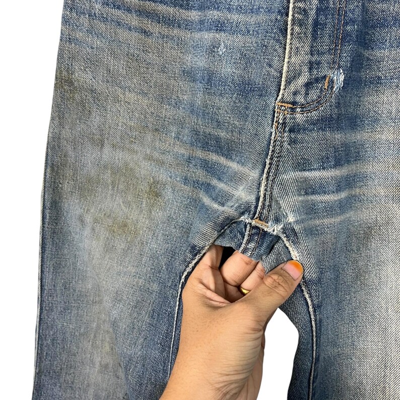 K&ouml;nnte beinhalten: Nahaufnahme einer hellblauen Jeans mit sichtbaren Gebrauchsspuren. Die Jeans weist Anzeichen von Ausbleichen und Verf&auml;rbungen auf und hat einen Used-Look. Das Bild hebt die Textur und Details des Stoffes hervor.