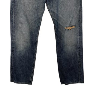 May include: A pair of blue denim jeans with a distressed knee. The jeans have a straight leg and a classic fit.