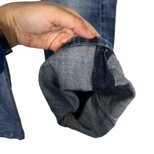 K&ouml;nnte beinhalten: Nahaufnahme einer blauen Jeans, die den umgeschlagenen Saum zeigt. Der Denim hat eine verwaschene Optik mit sichtbaren N&auml;hten und einem klassischen Design. Der Saum zeigt das Innenfutter und Konstruktionsdetails.