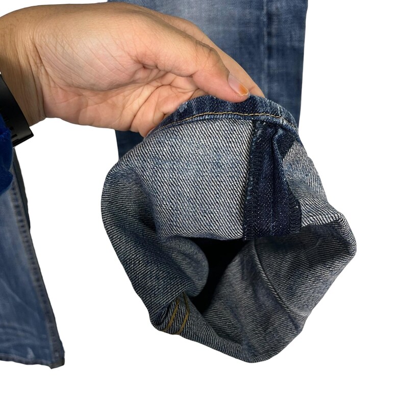 K&ouml;nnte beinhalten: Nahaufnahme einer blauen Jeans, die den umgeschlagenen Saum zeigt. Der Denim hat eine verwaschene Optik mit sichtbaren N&auml;hten und einem klassischen Design. Der Saum zeigt das Innenfutter und Konstruktionsdetails.