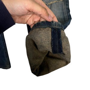 May include: Close-up of denim jeans with a folded cuff. The cuff reveals a textured, tan interior with a dark blue stripe. The jeans have a faded blue wash and a classic design.