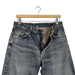 May include: A pair of blue denim jeans with a zip fly and a button fastening. The jeans have a faded and distressed look, with visible wear and tear.