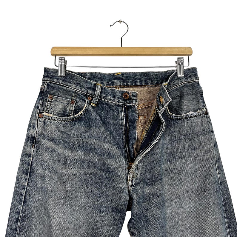 May include: A pair of blue denim jeans with a zip fly and a button fastening. The jeans have a faded and distressed look, with visible wear and tear.