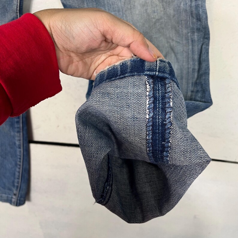 Puede incluir: Primer plano del dobladillo de unos vaqueros de mezclilla azul claro. El pu&ntilde;o est&aacute; doblado, revelando el interior de la mezclilla y los detalles de las costuras. Los vaqueros parecen desgastados y descoloridos.