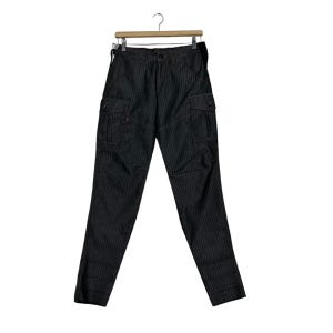 Puede incluir: Pantalones cargo grises oscuros con finas rayas verticales, con múltiples bolsillos y cierre de botón. Los pantalones cuelgan de una percha de madera sobre un fondo blanco. Los pantalones tienen un diseño clásico y utilitario.