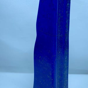 Op de afbeelding: Een hoge, gepolijste lapis lazuli stenen toren met een diepe koningsblauwe kleur en zichtbare natuurlijke gouden pyrietspikkels over het hele oppervlak. De steen heeft een gladde, verticale, licht onregelmatige vorm met een afgeronde bovenrand.