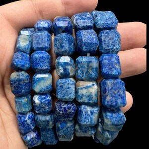 Könnte beinhalten: Eine Strähne aus blauen und weißen Lapislazuli-Perlen, jede Perle ist facettiert und hat eine quadratische Form.