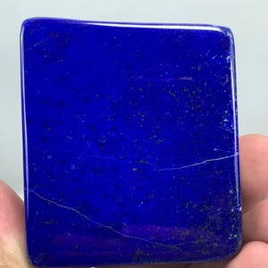 Peut inclure: Une dalle rectangulaire de lapis-lazuli poli présentant une couleur bleu roi profond avec des inclusions naturelles de paillettes de pyrite dorées et de fines veines minérales blanches traversant la surface lisse et plate.