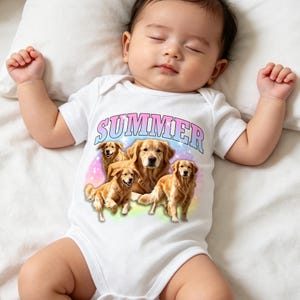 May include: A white short-sleeved baby bodysuit featuring a graphic print of three golden retriever dogs against a colourful, starry background. The word SUMMER is printed in a large, arched, blue-to-pink gradient font above the dogs.