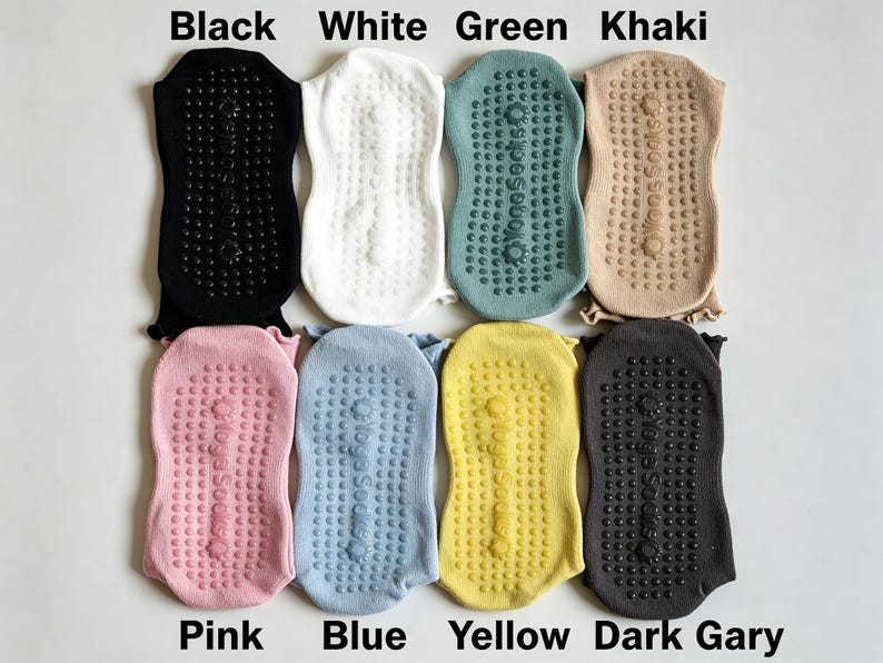May include: Eight pairs of yoga socks arranged in two rows, featuring colors black, white, green, khaki, pink, blue, yellow, and dark gray. Each sock has a textured grip pattern on the sole with the text Yoga Socks printed in the center.