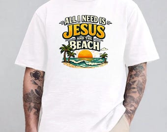 May include: A white short-sleeve t-shirt featuring a graphic print with the text "ALL I NEED IS JESUS AND THE BEACH" in yellow and black lettering, accompanied by an illustration of a sunset, ocean waves, and palm trees on a sandy shore.