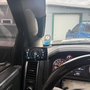 Peut inclure: Intérieur de voiture noir avec un affichage numérique de jauge indiquant une vitesse de 100 mph et un niveau de carburant de 63%. La jauge est montée sur le tableau de bord près du volant.