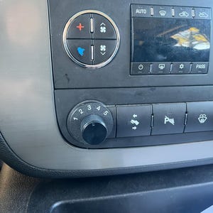 May include: A car's dashboard with a black and silver control panel. The panel has buttons for climate control, including temperature, fan speed, and air direction. There are also buttons for other functions, such as the radio, navigation, and phone.