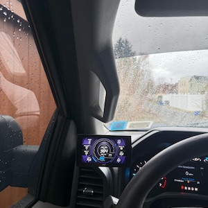 May include: A black dashboard gauge with a digital display showing a speed of 984 mph. The gauge is mounted in a car's interior and has a blue and purple colour scheme.